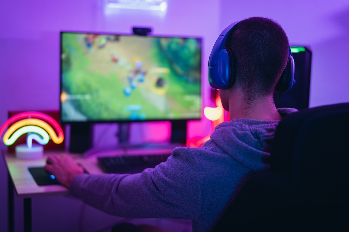 Young male gamer with headphones facing large monitor