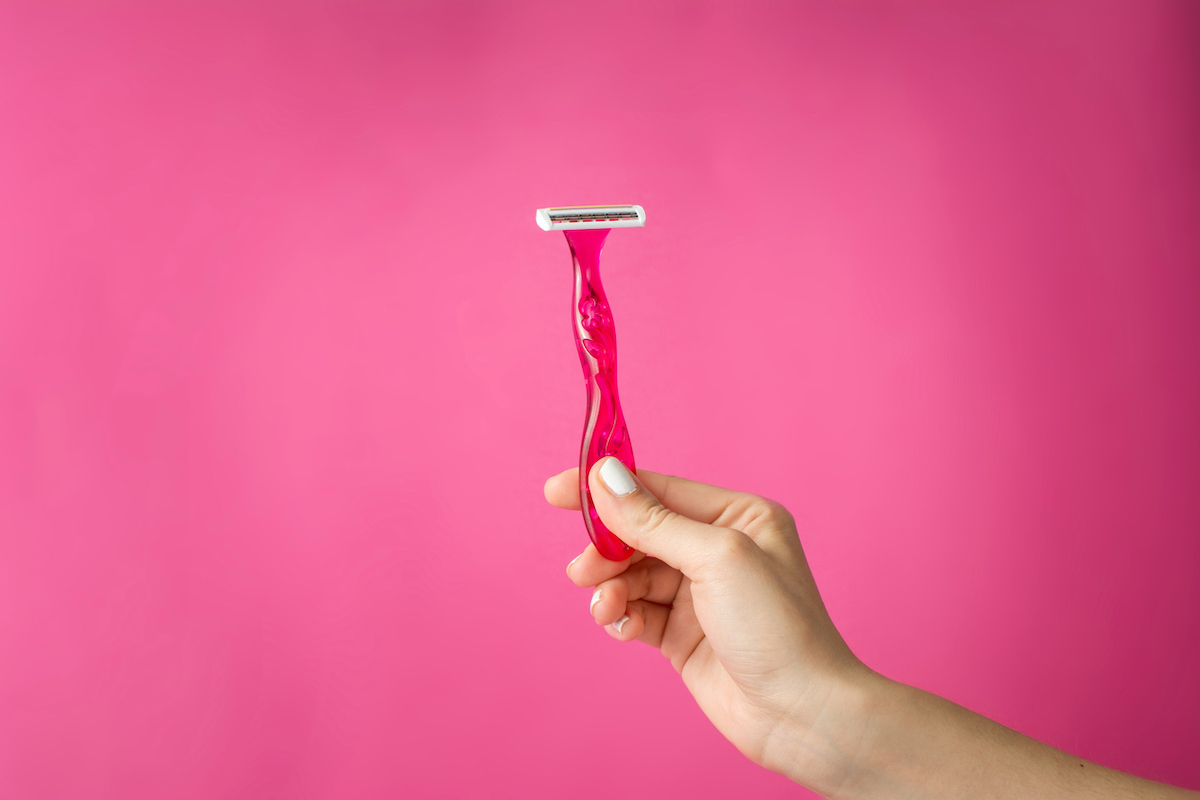 Red shaver in woman hands against pink background