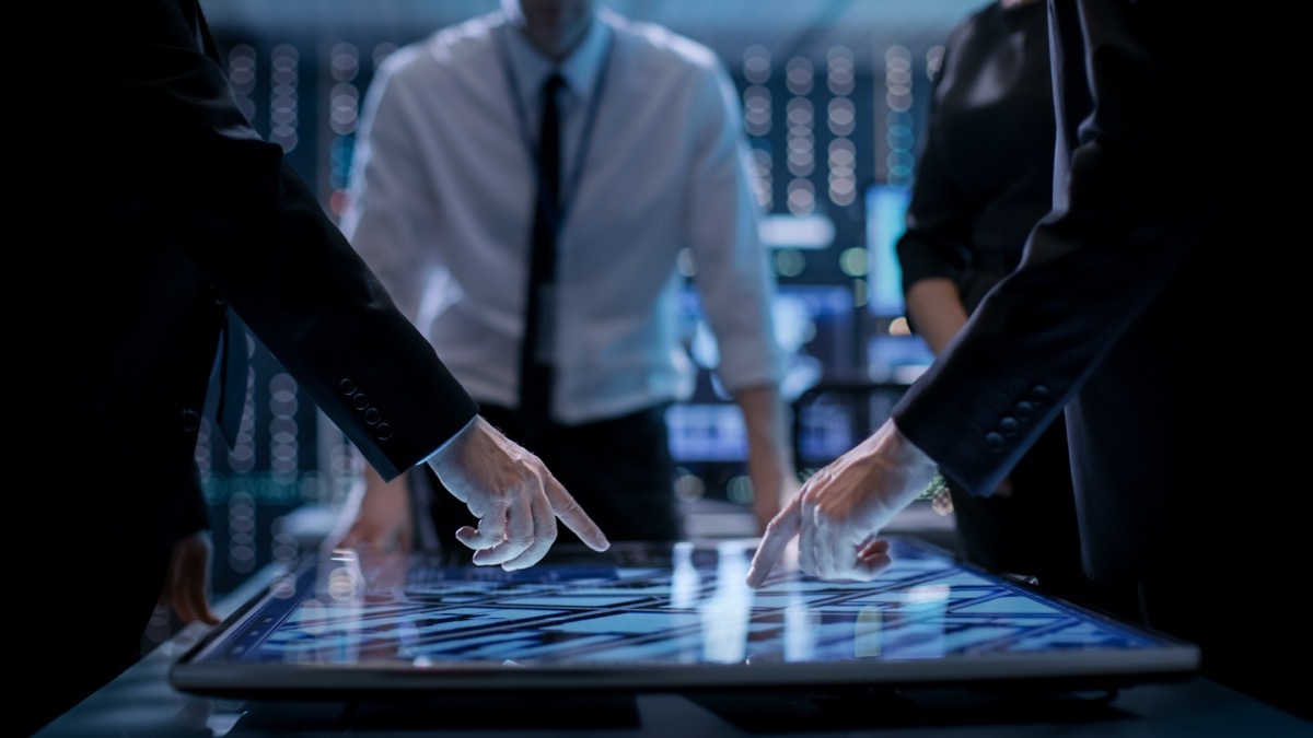 Corporate Managers Working at the Table in Monitoring Room. Room is Full of State of the Art Technology. Computers with Animated Screens. - Image