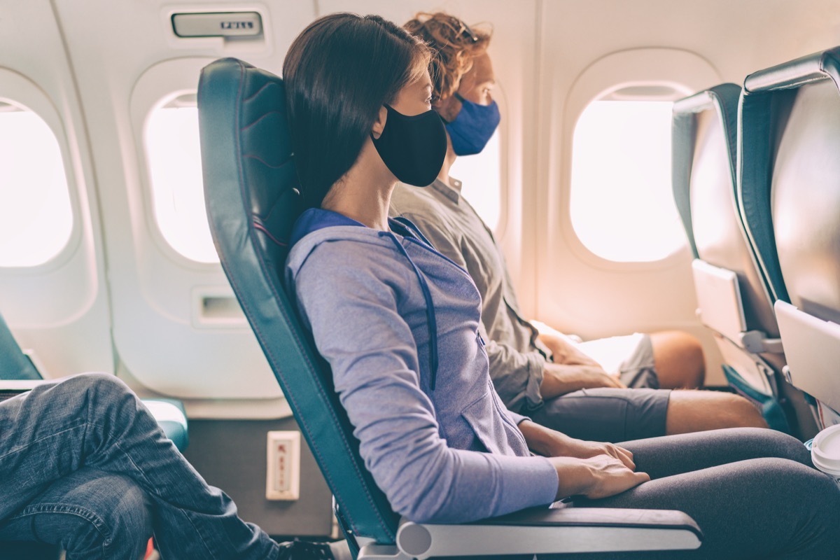 Couple tourists wearing face masks on travel vacation flight inside plane. Coronavirus safety prevention for passengers of flight. People lifestyle.