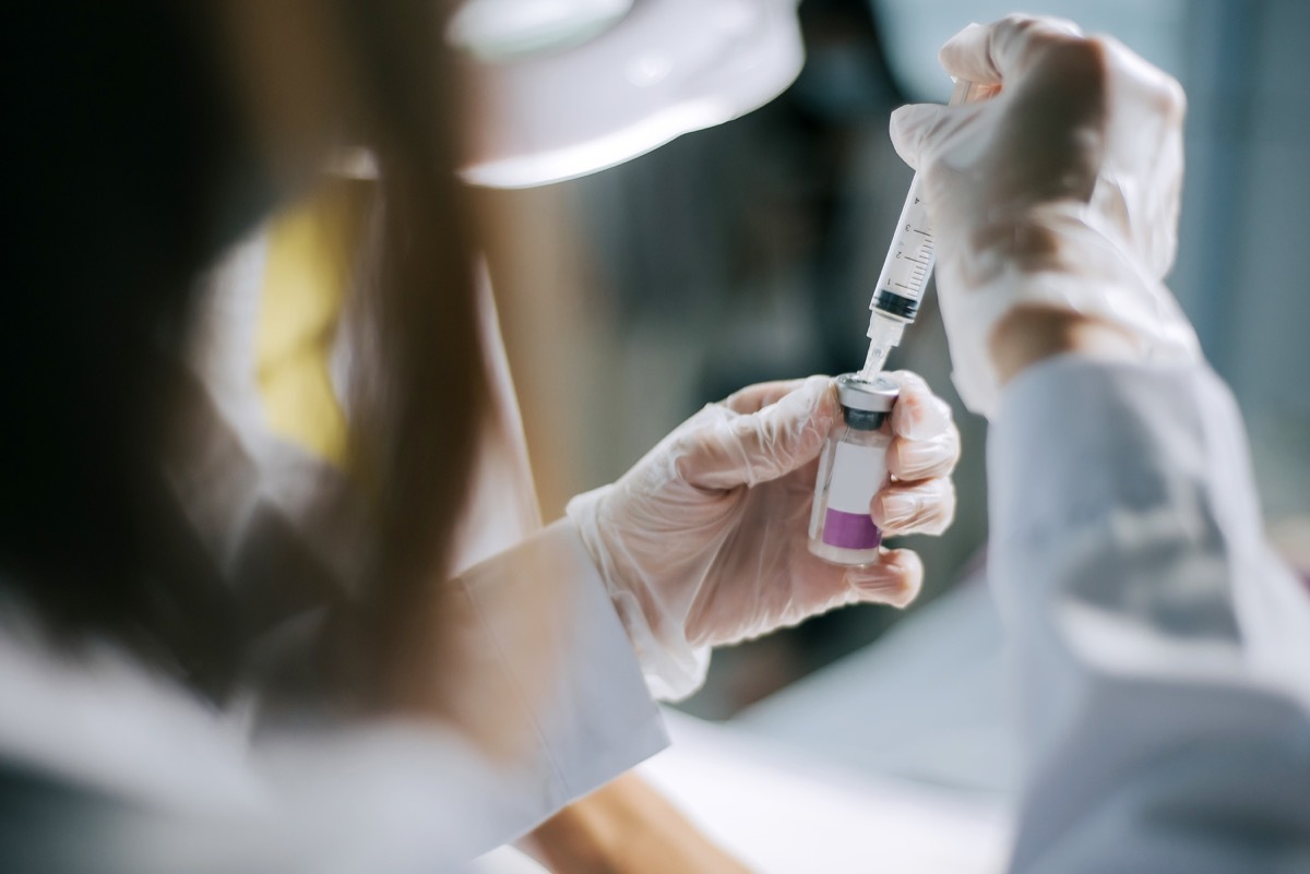 rear view of hand holding syringe and covid-19 vaccine