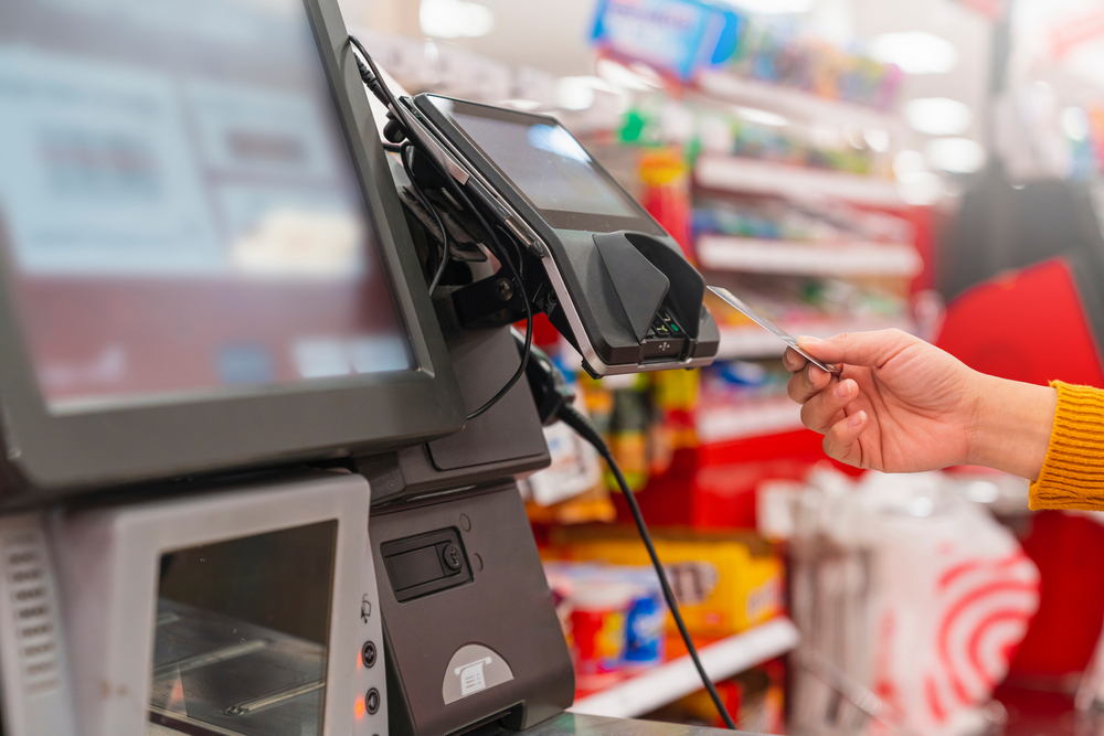 A close up of a person using a self-checkout register and paying with a credit card