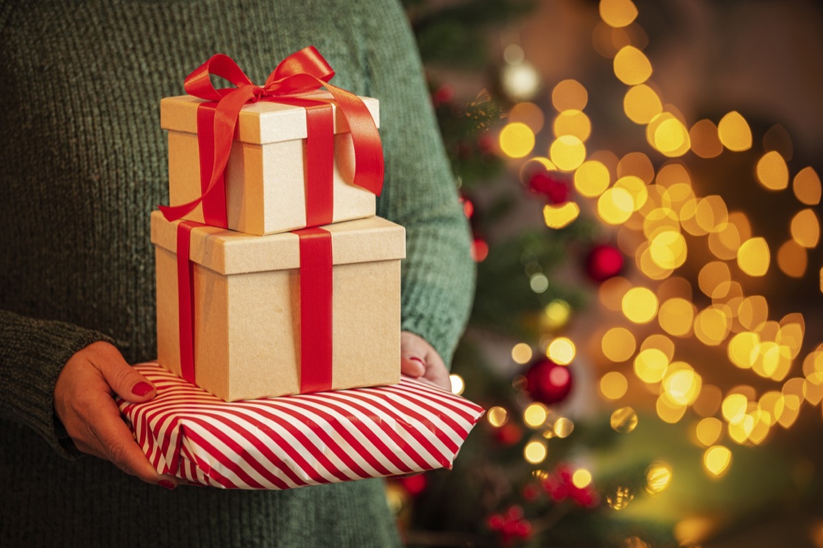 Close up view of woman's hands holding three Christmas presents with defocused Christmas tree and string lights at background. High resolution 42Mp outdoors digital capture taken with SONY A7rII and Canon EF 70-200mm f/2.8L IS II USM Telephoto Zoom LensOSS lens