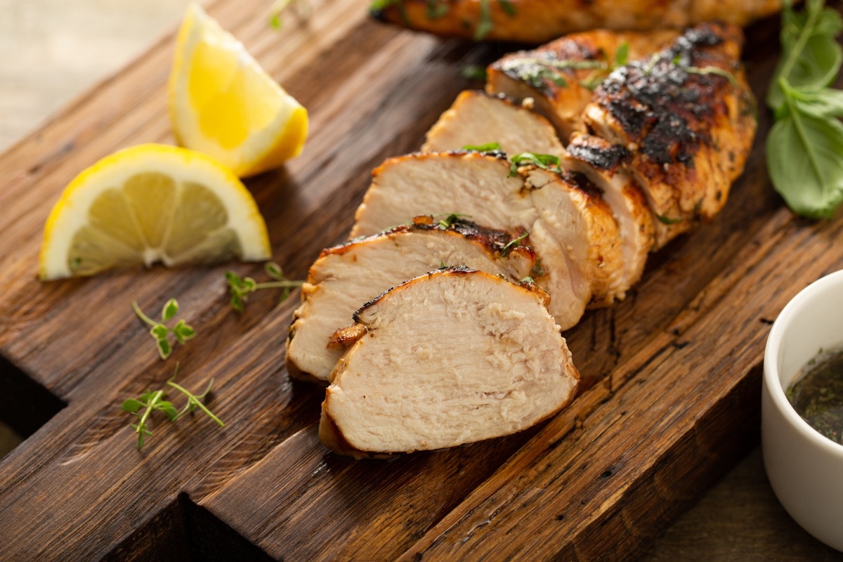 grilled chicken breast with fresh herbs sliced on a rustic wooden board