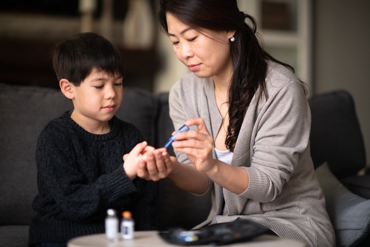 A mother and son are sitting together in a living room. She is helping him check his blood sugar levels because he is diabetic.