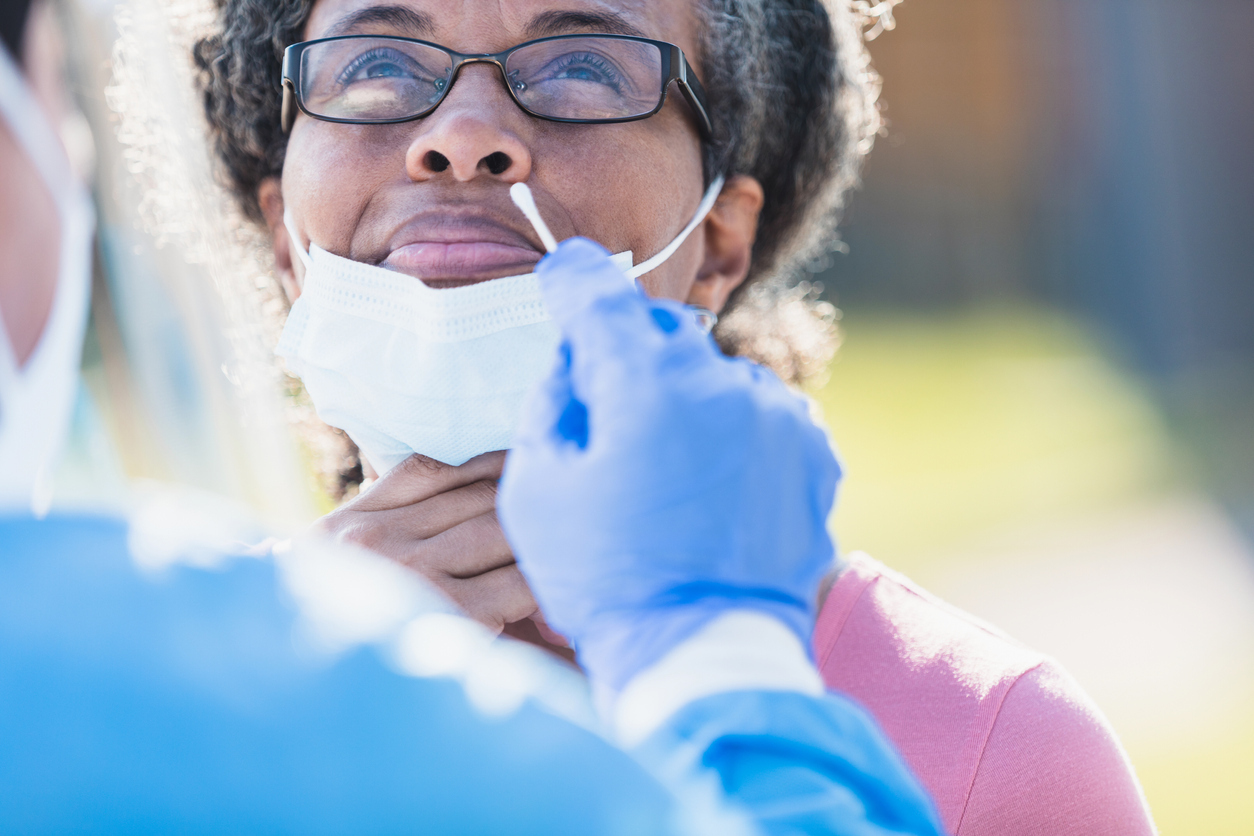 A middle-aged woman pulls down her face mask to receive a nasal swab for a COVID-19 test.