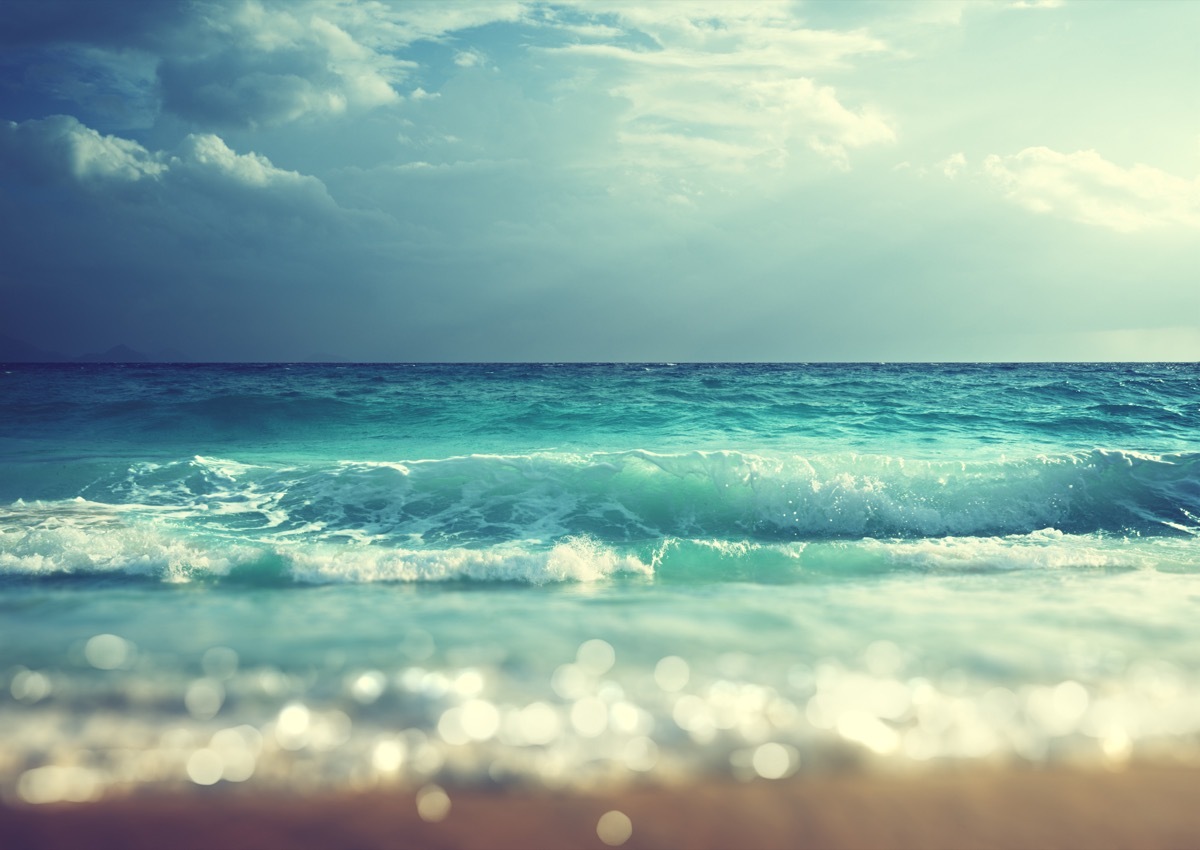 blue waves crashing on a beach, dark sky in the distance