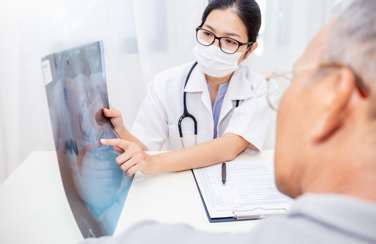 Portrait of woman doctor wear protection face mask show patient some information on digital tablet clip board, patient listen to specialist doctor in clinic office. Epidemic flu or Coronavirus.