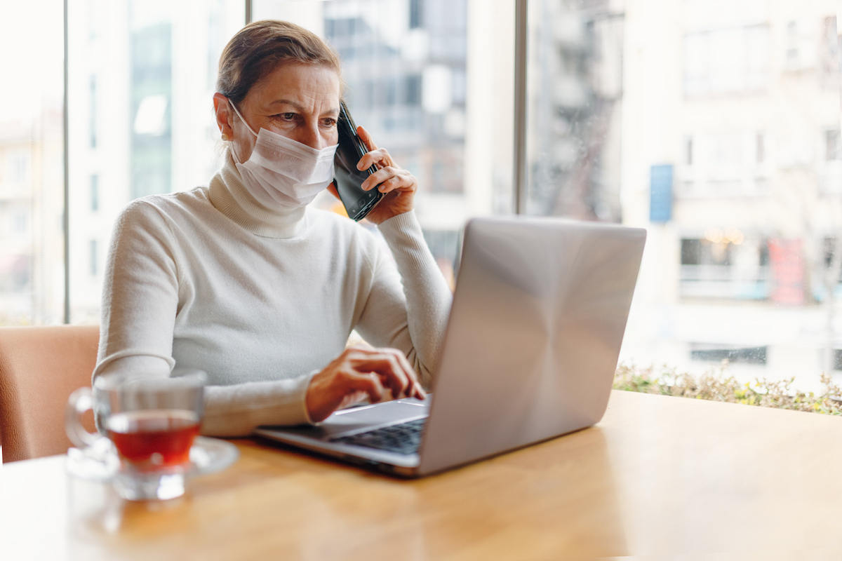 senior Woman With Face Mask, sitting at computer while on the phone