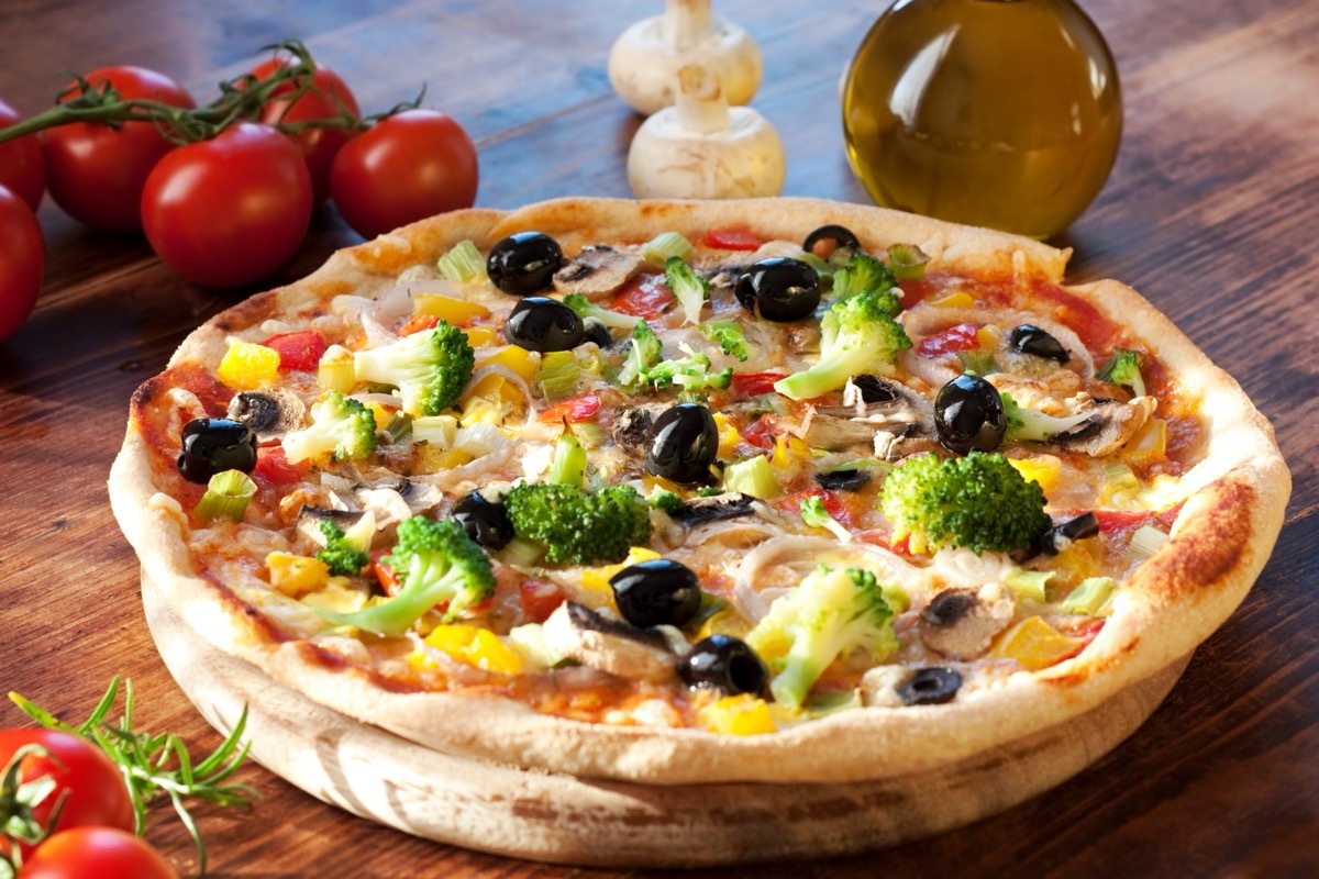 Veggie Pizza on a wood table surrounded by fresh tomatoes