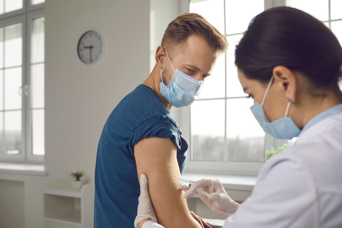 Young guy in medical face mask getting COVID-19 vaccine shot at the hospital. 