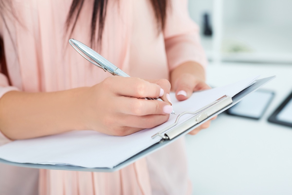 woman in pink shirt writing on clipboard