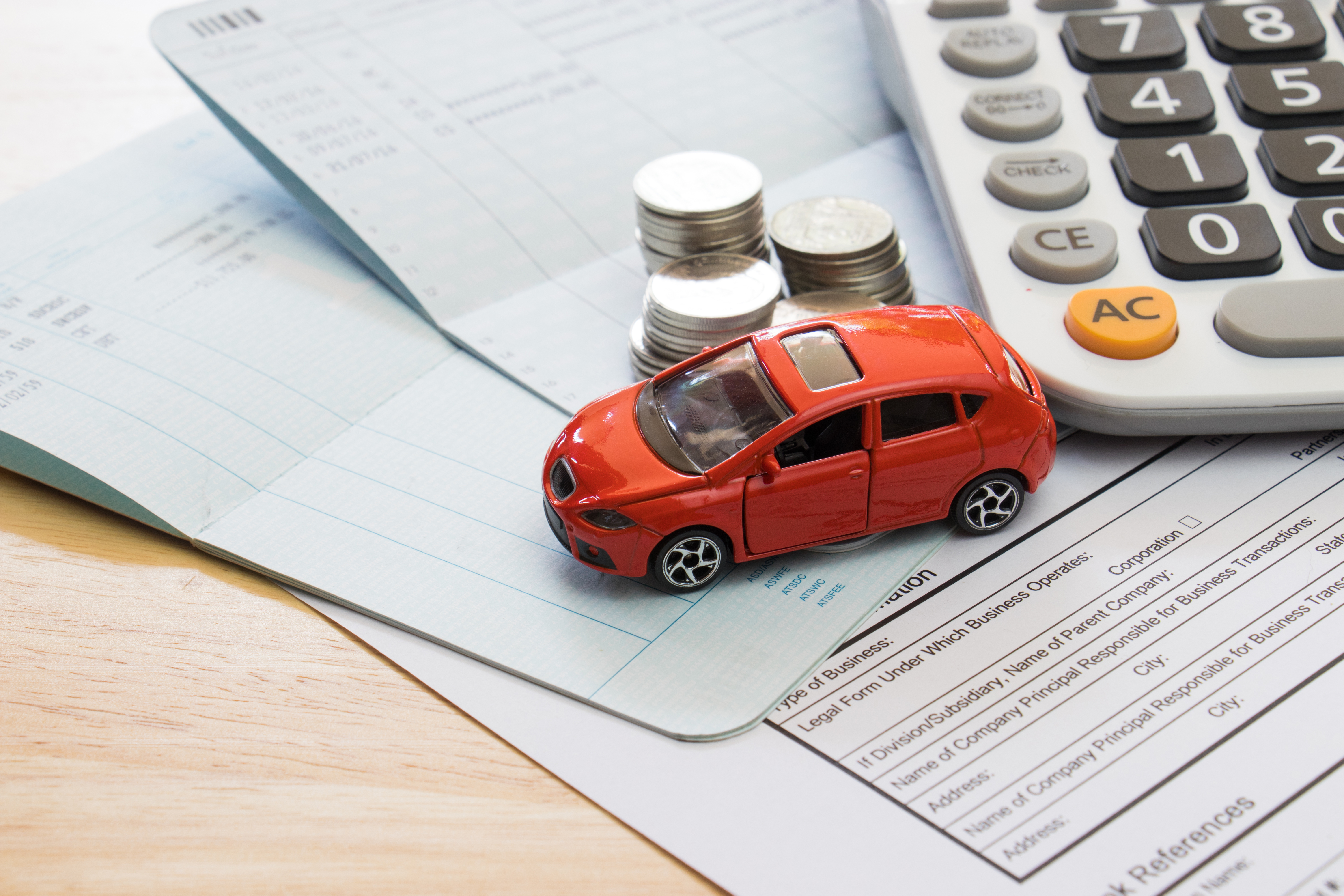 calculator, stacks of quarters, and toy car sitting on bills on wooden table