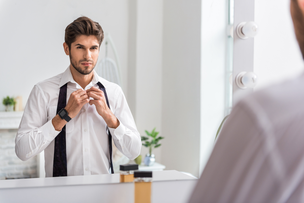 confident man putting on tie in mirror