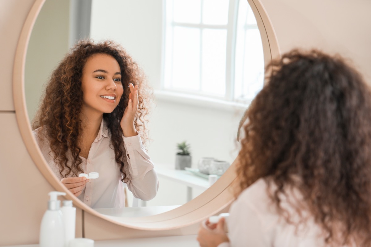 Young African-American woman putting in contact lenses at home