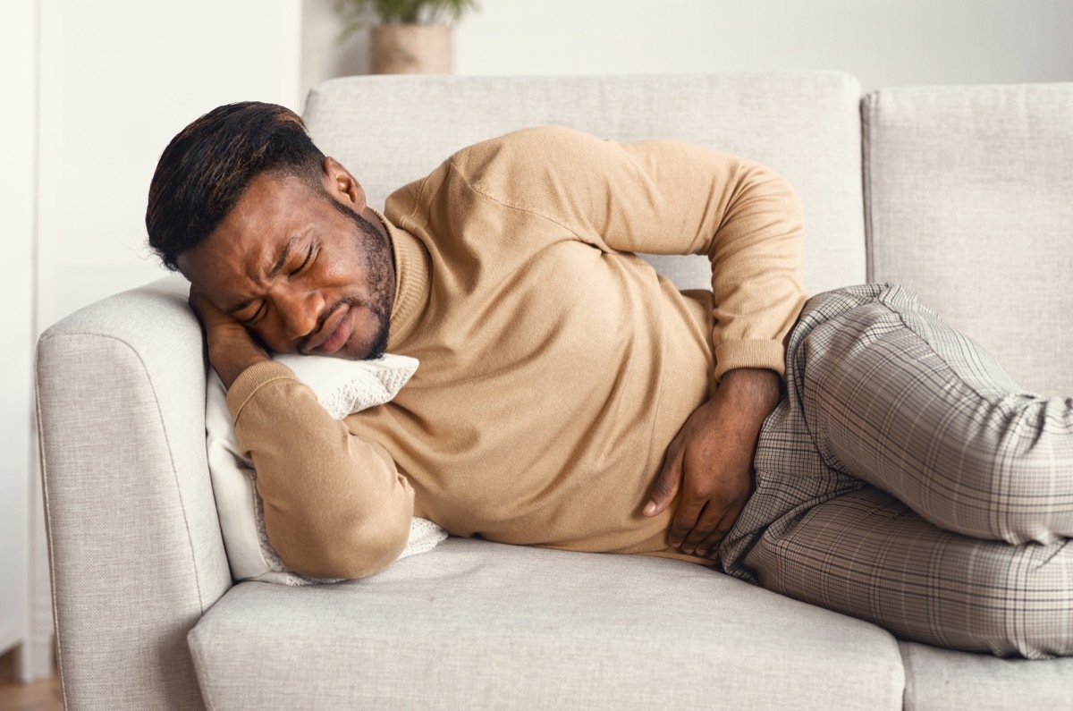 man sitting on a couch in pain, abdominal pain, hand on stomach, looking uncomfortable