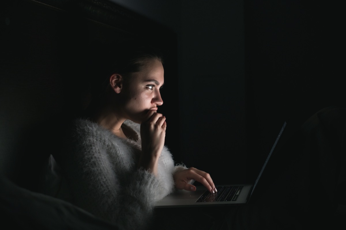 young girl sits in the dark at night, enthusiastically watches TV series on laptop