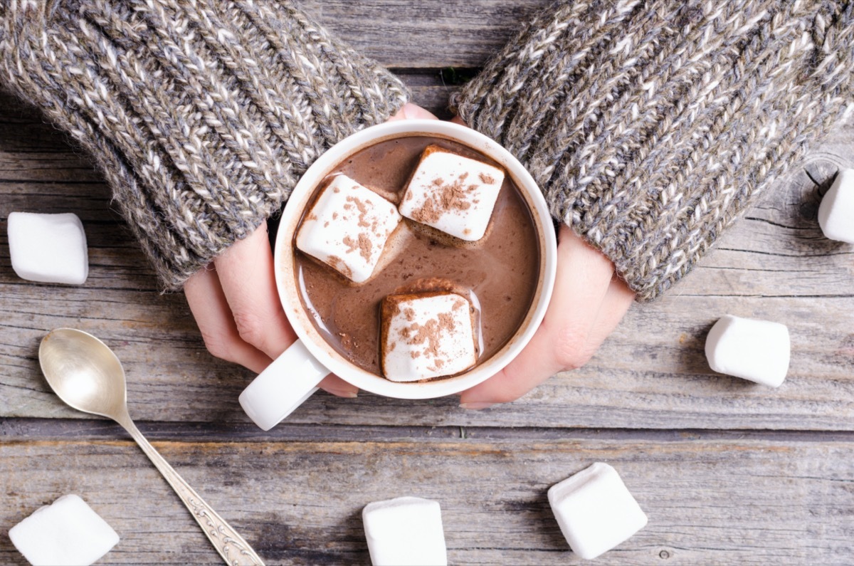 person wearing gray sweater holding mug of hot chocolate