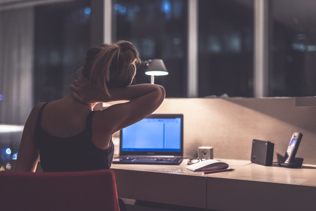 Young exhausted,depressed,concentrated woman sitting in her room or office with french windows in the dark at the lamp