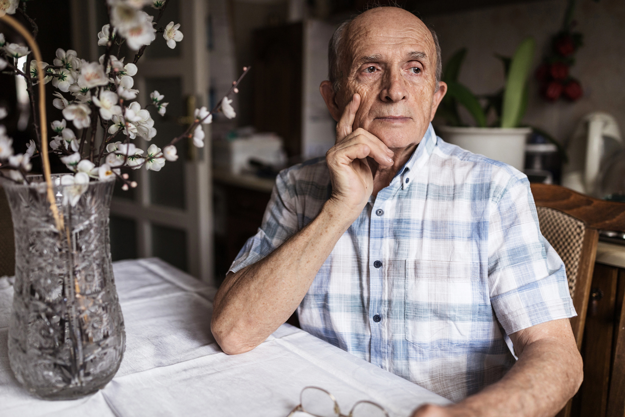 A senior man sitting at a table with a worried look on his face.