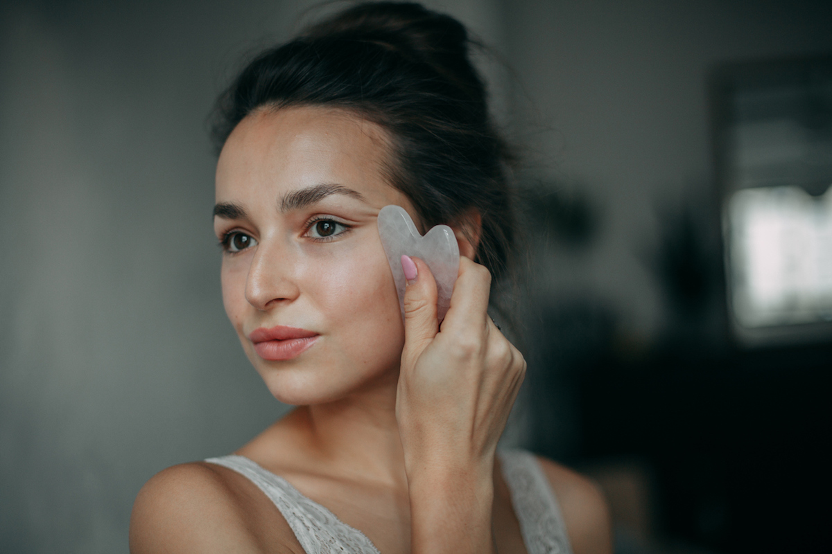 Portrait of a young woman using a gua sha tool on her face