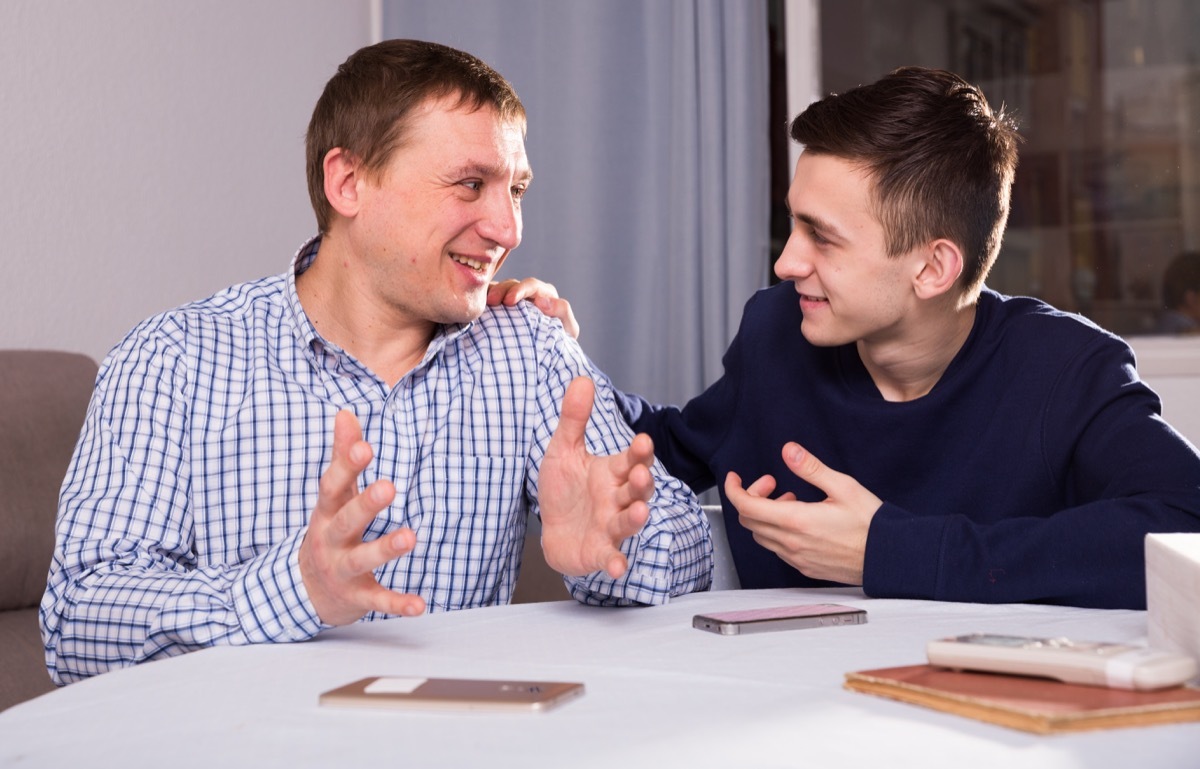 father and son sitting at table with smartphones on it