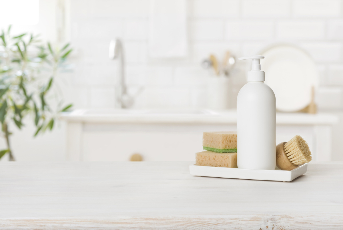 White plastic dishwashing gel bottle with sponges on kitchen table