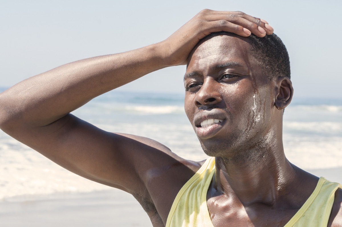 close up of black man sweating outside with his hand on his forehead