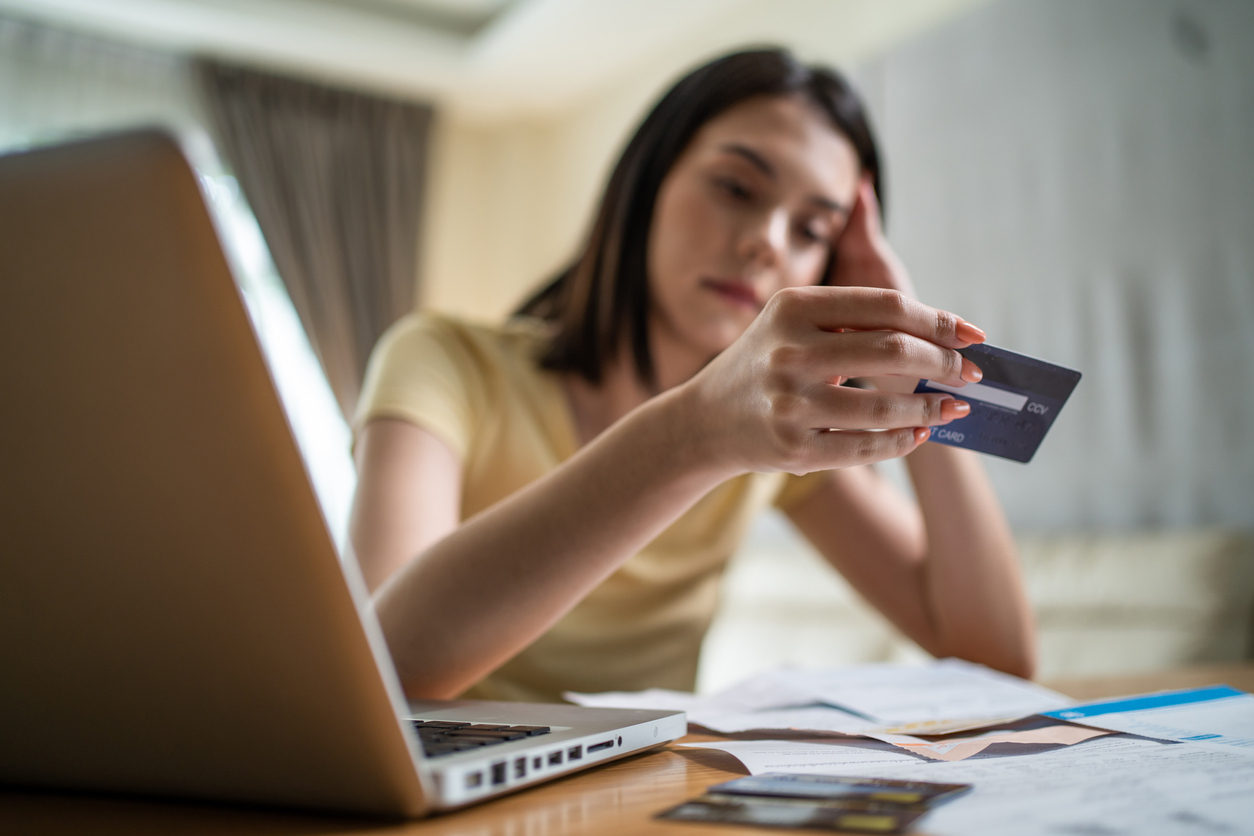 A young woman holding a credit card at her desk and looking at it with a sad expression