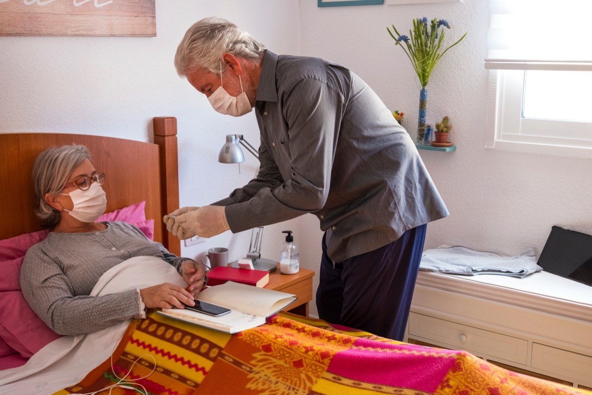 older man caring for woman with covid wearing mask in bed