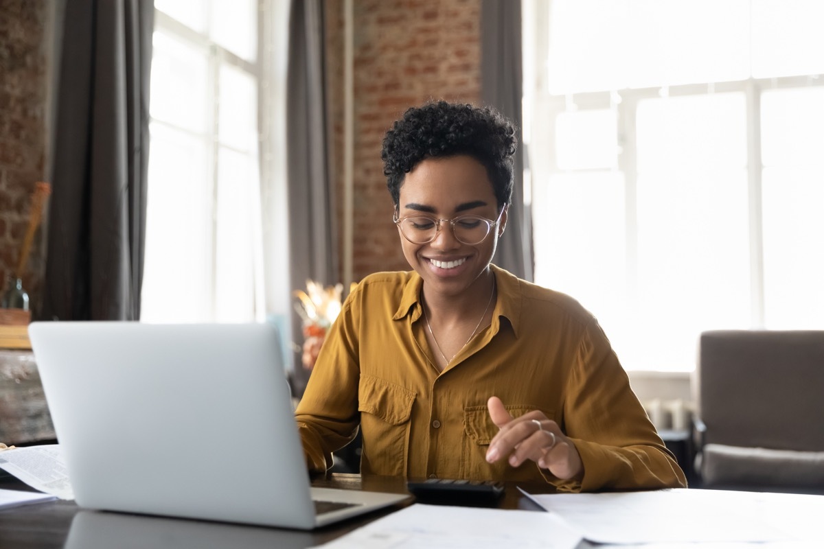 entrepreneur woman in glasses counting profit, on calculator at laptop computer, analyzing benefits, enjoying financial success, job high result, smiling