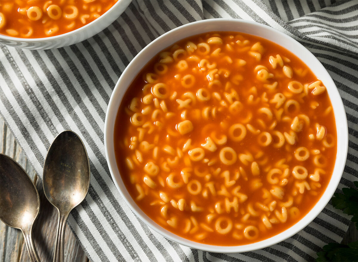 bowl of alphabet soup with spoons on striped tablecloth