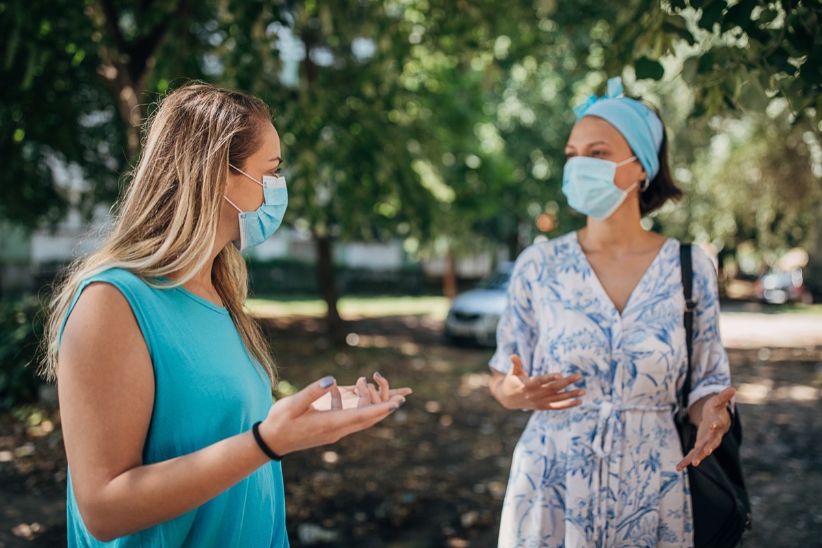 Two women with protective face masks talking on the city street in safe distance.