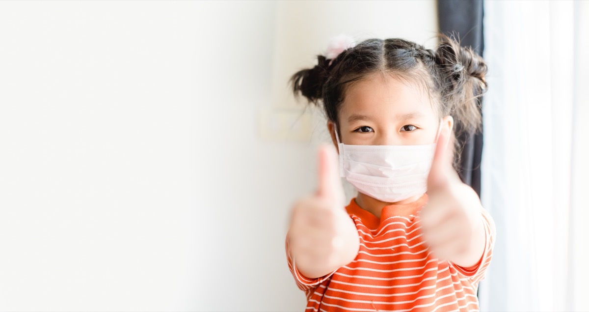 Child wearing a mask giving a thumbs up