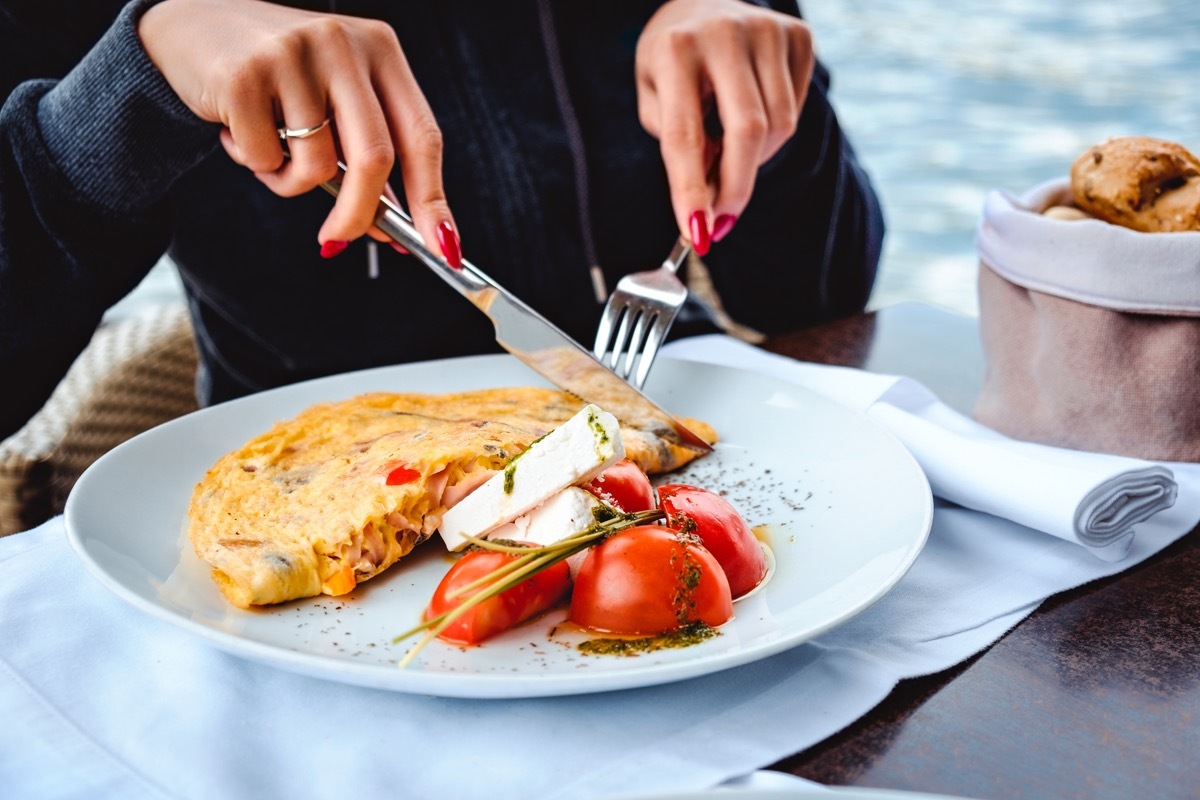 Woman eating scrambled eggs, cheese, tomatto and bread in restaurant by the water