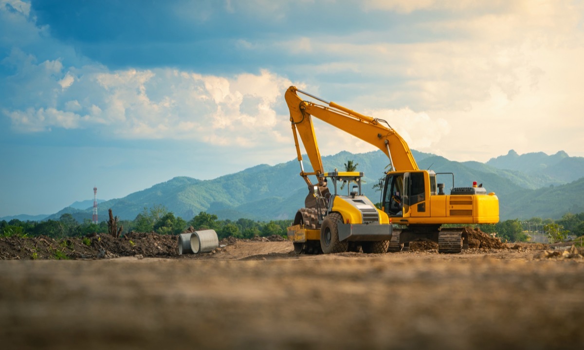 Backhoe working in road construction site, with mountains and sky