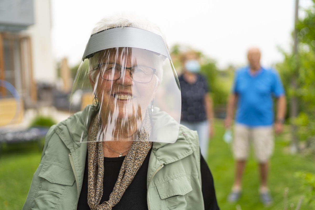 older white woman smiling behind a face shield outside