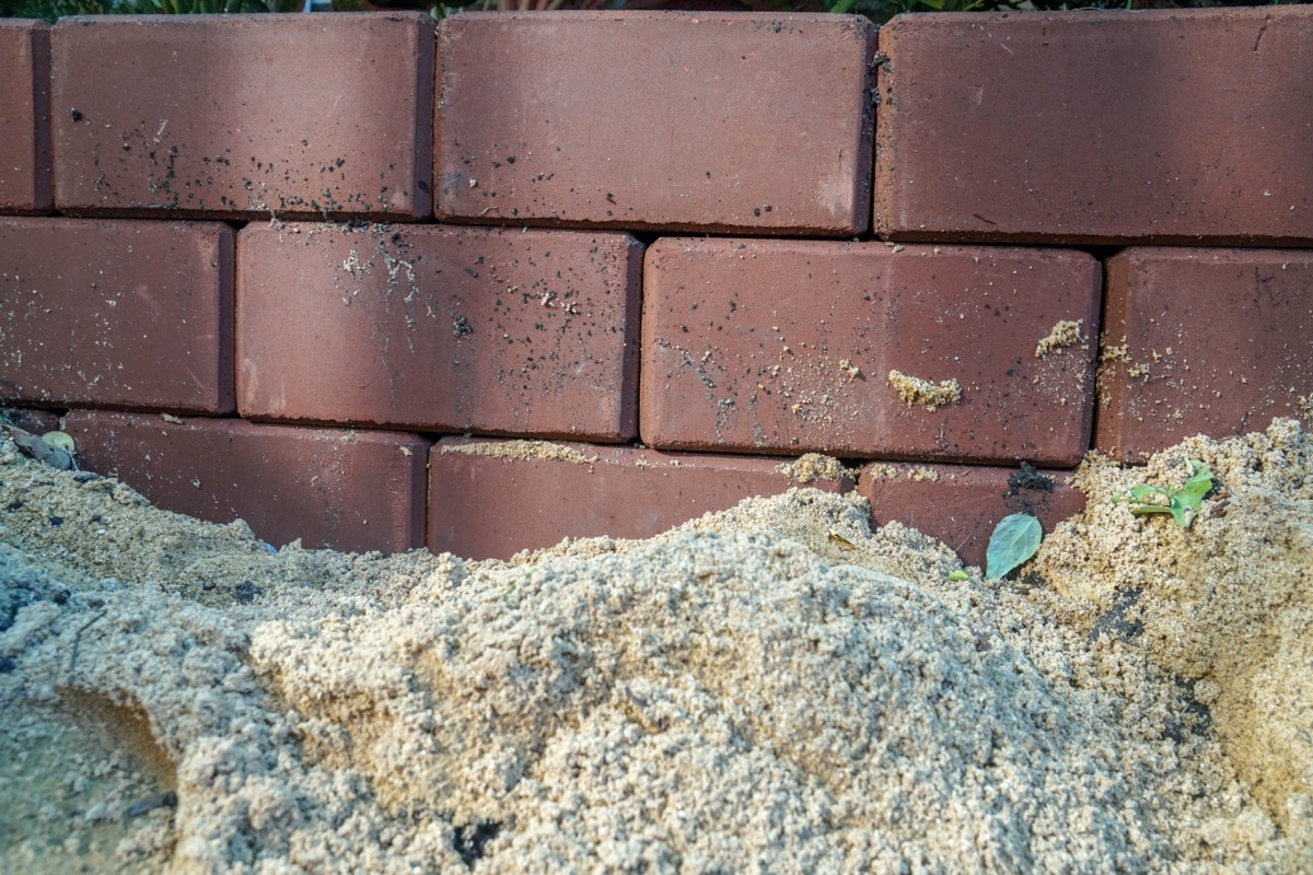 pile of dirt next to the brick foundation of a home