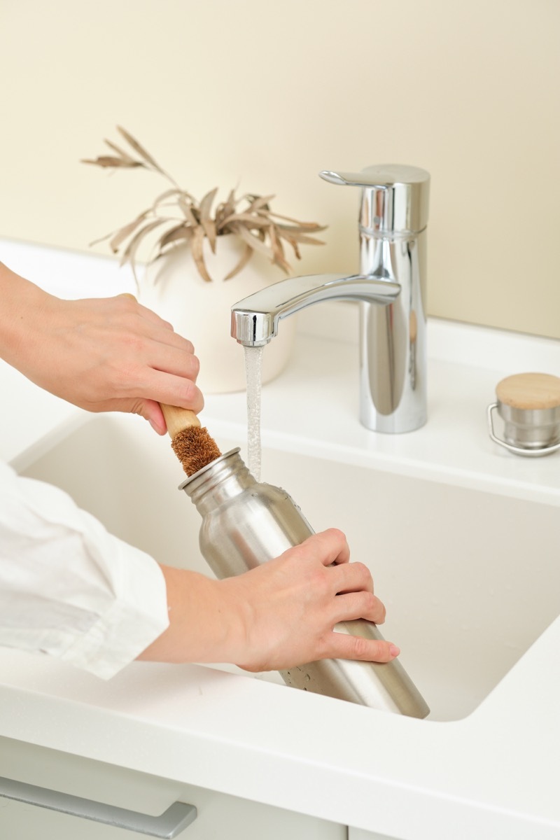 Woman washing a steel water bottle in the sink