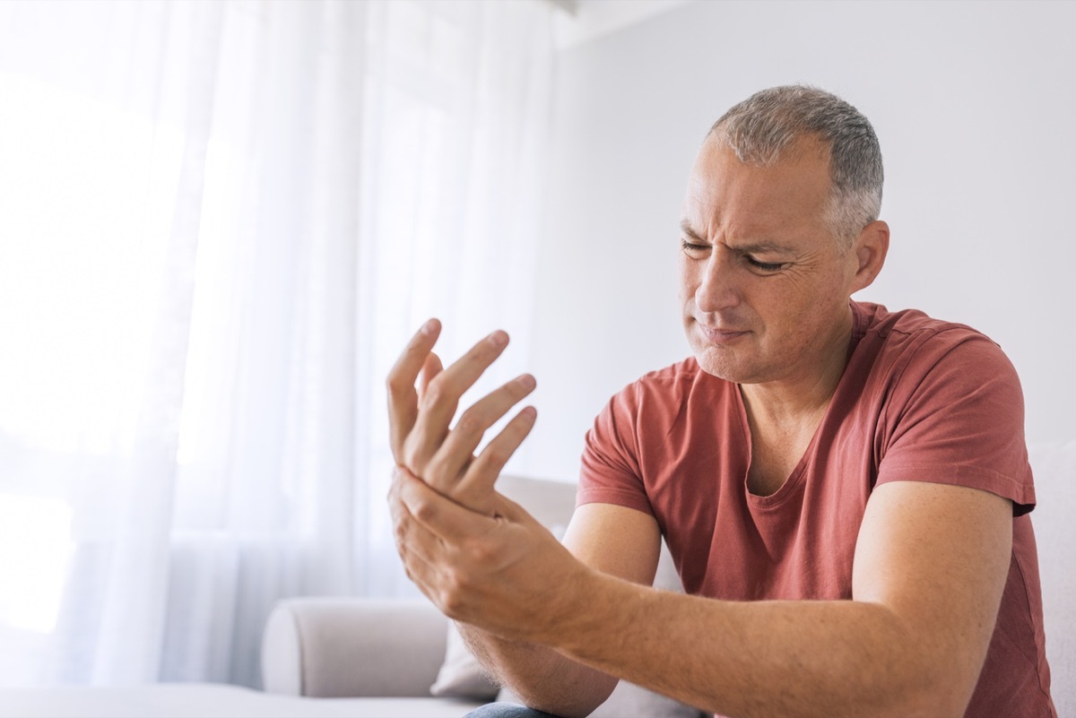 Mature man suffering from wrist pain at home while sitting on sofa during the day