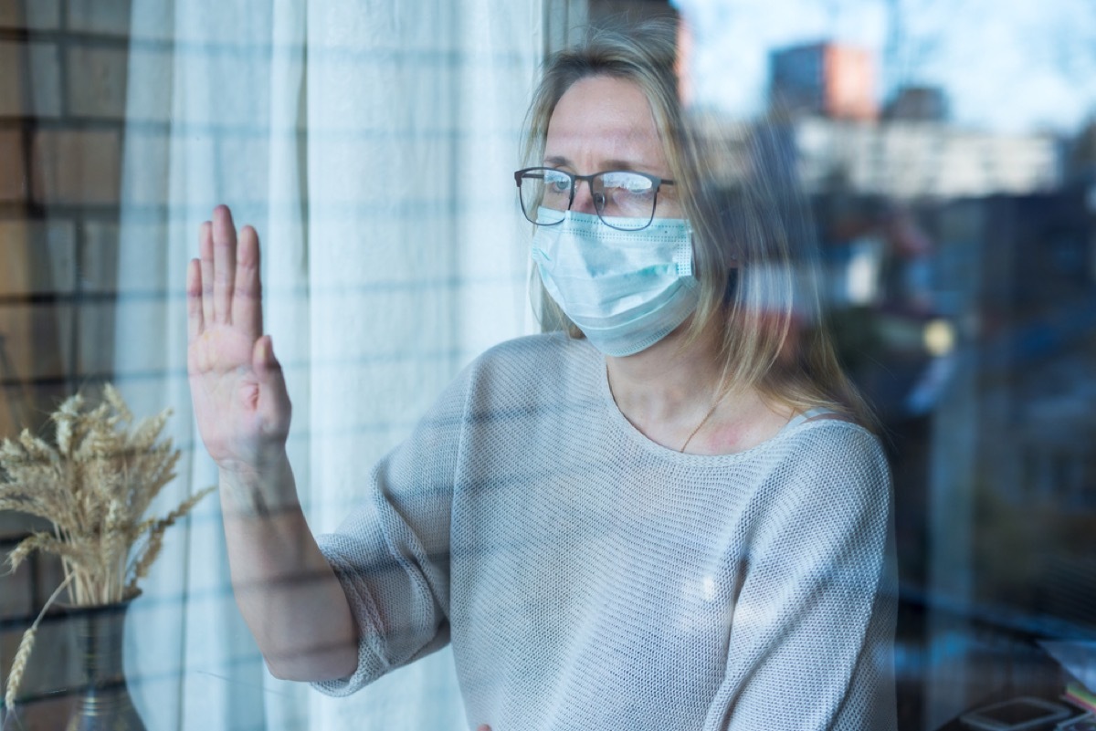 woman with face mask pressing her hand against the window