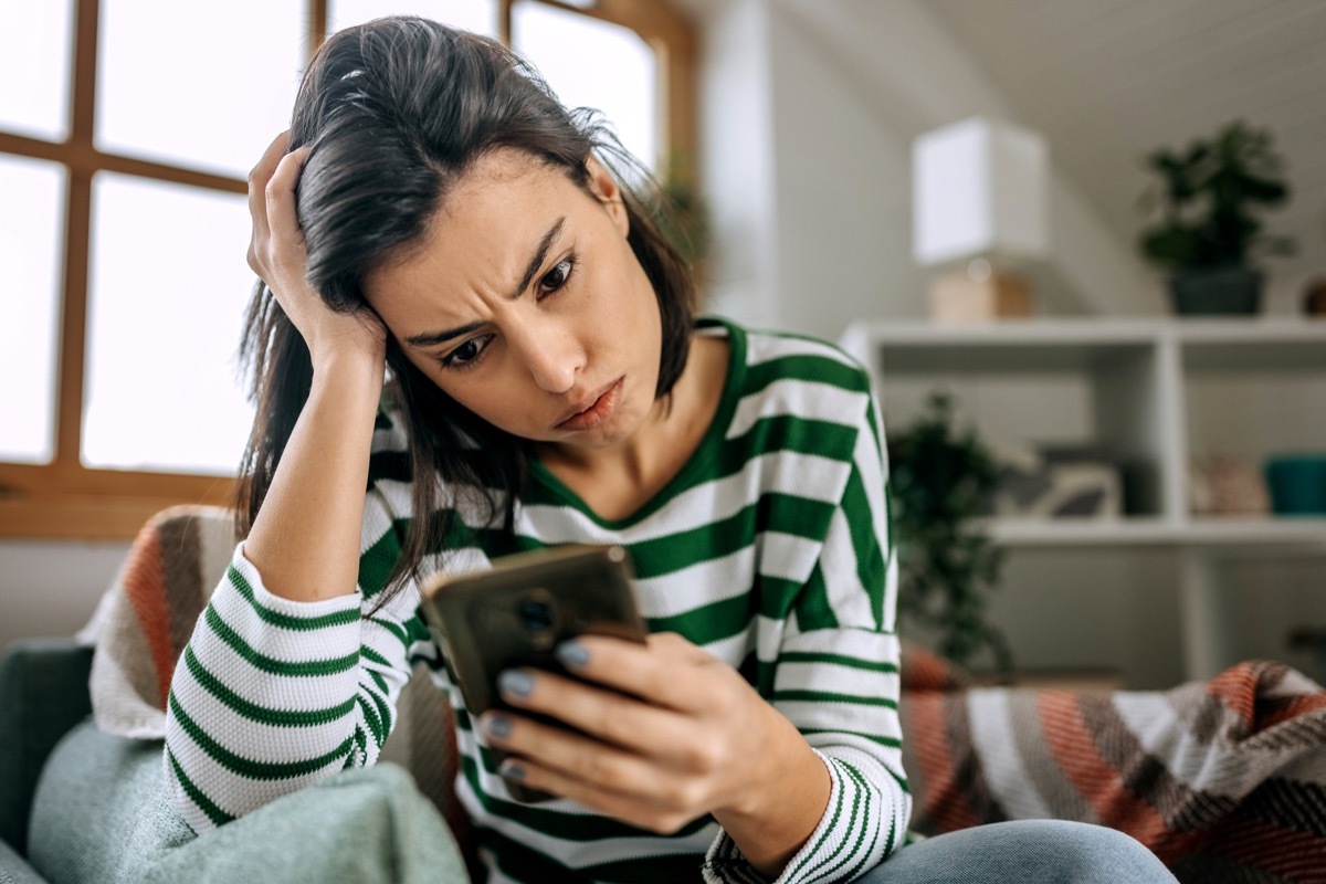 Frustrated woman using mobile phone while sitting on sofa