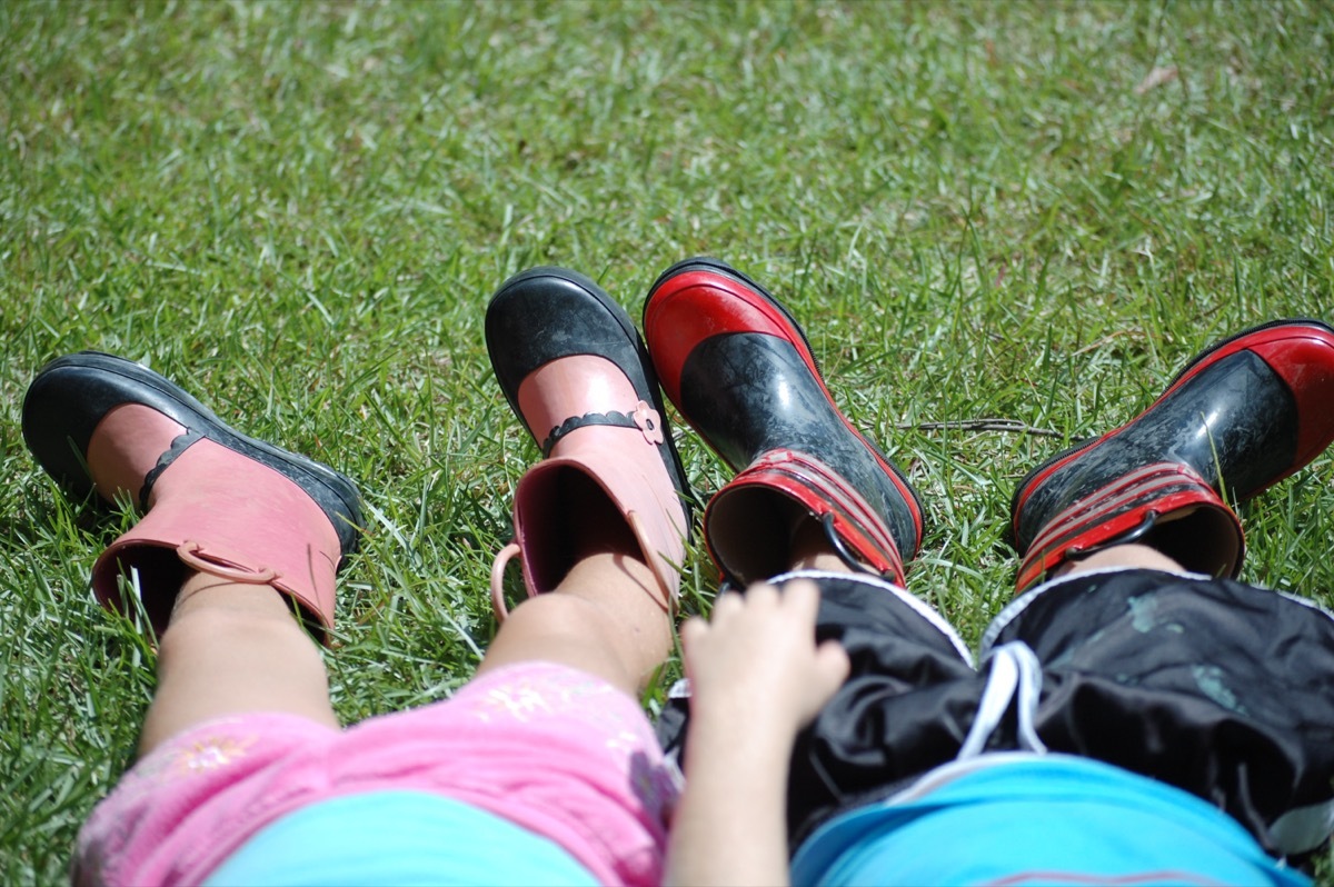 Young boy and girl laying in grass wearing fun rain boots.