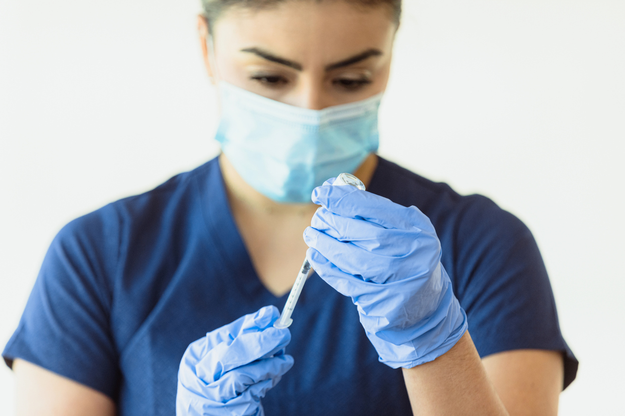 A female healthcare workers fills a syringe with COVID-19 vaccine