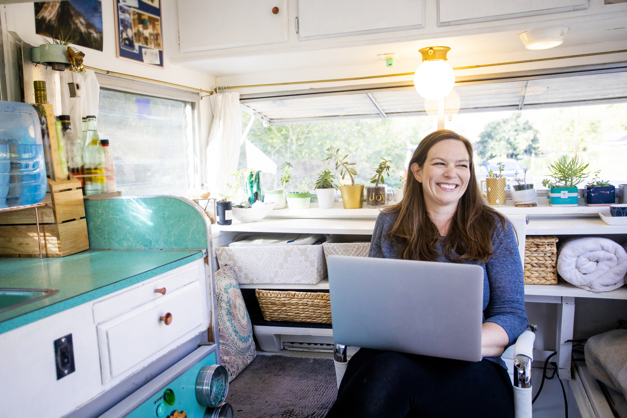 A young woman sitting on her laptop while smiling in her RV or tiny home