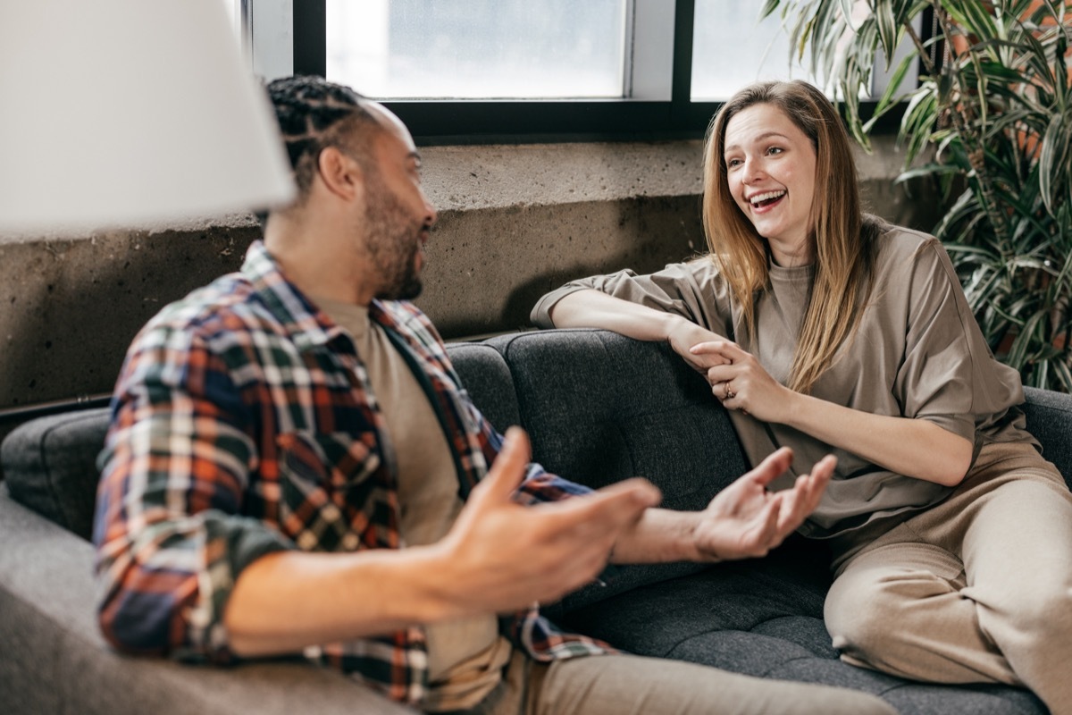 A young man and a lovely woman are seated on a couch, engaging in an upbeat conversation