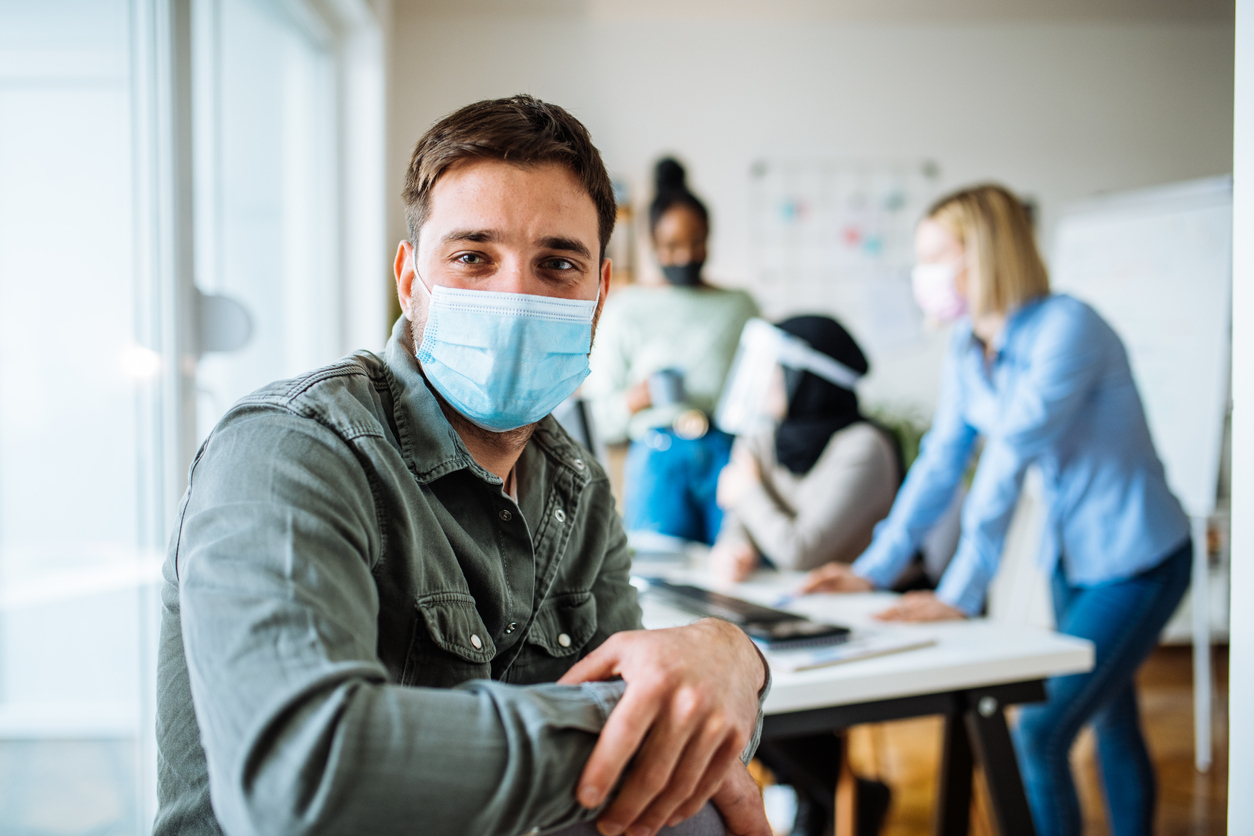 A young man wearing a protective face mask while sitting in his office