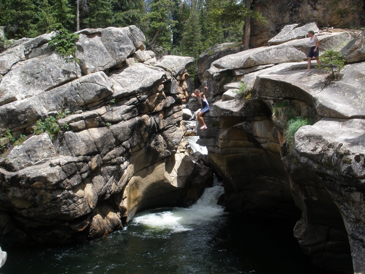 man jumps into a swimming hole surrounded by rocks in colorado