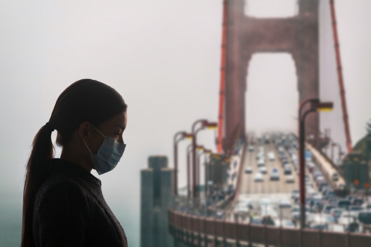 Woman with surgical mask for corona virus covid-19 protection in San Francisco, USA, in front of Golden Gate Bridge. California