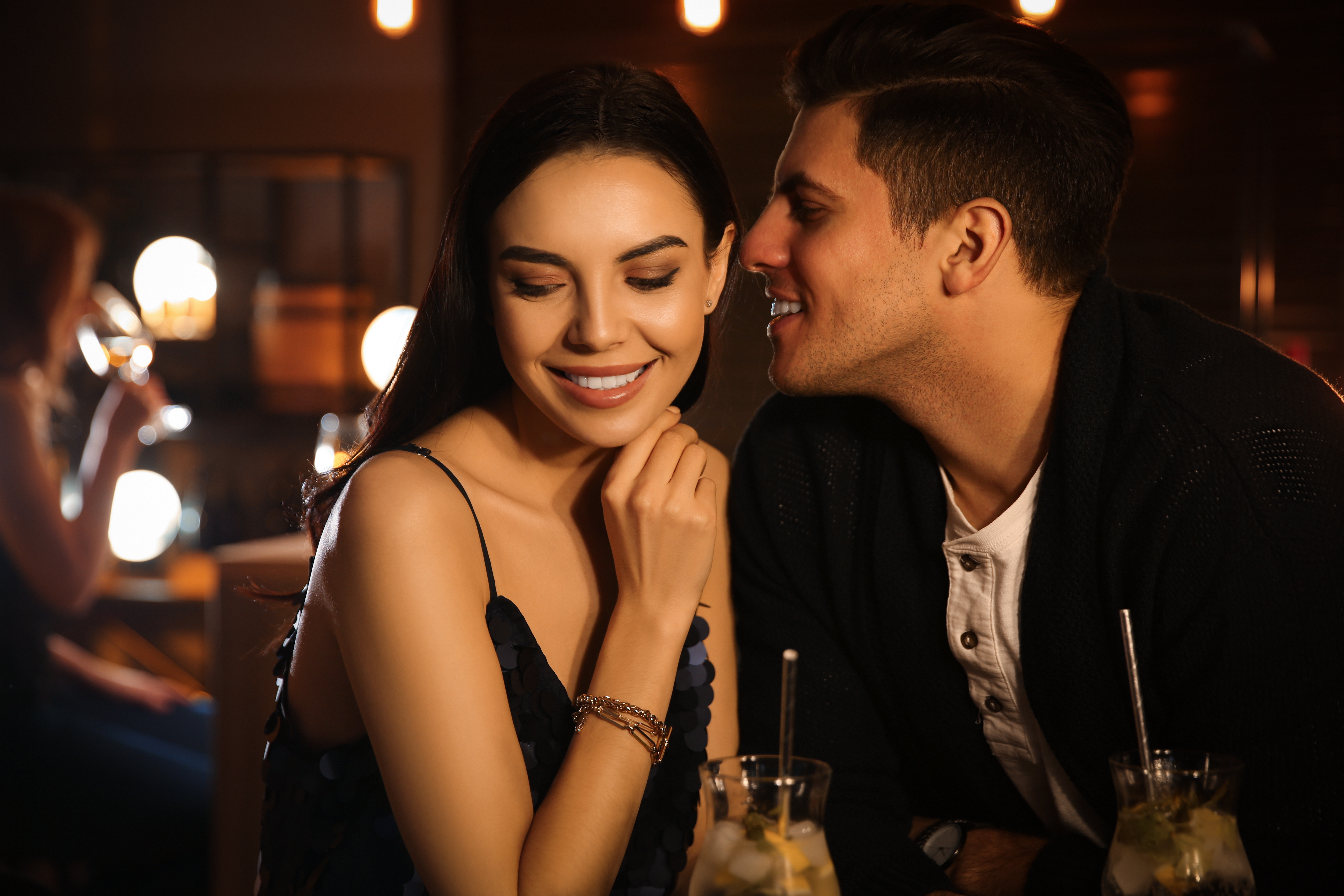 man whispering to woman at bar